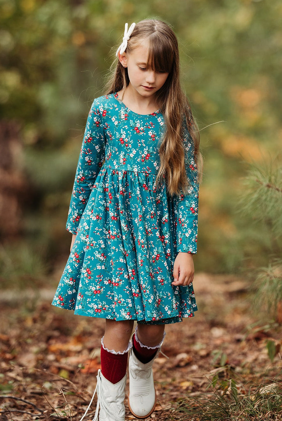 Young girl in a teal twirl dress with winter berry print standing in a forest
