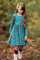 Young girl in a teal twirl dress with winter berry print standing in a forest