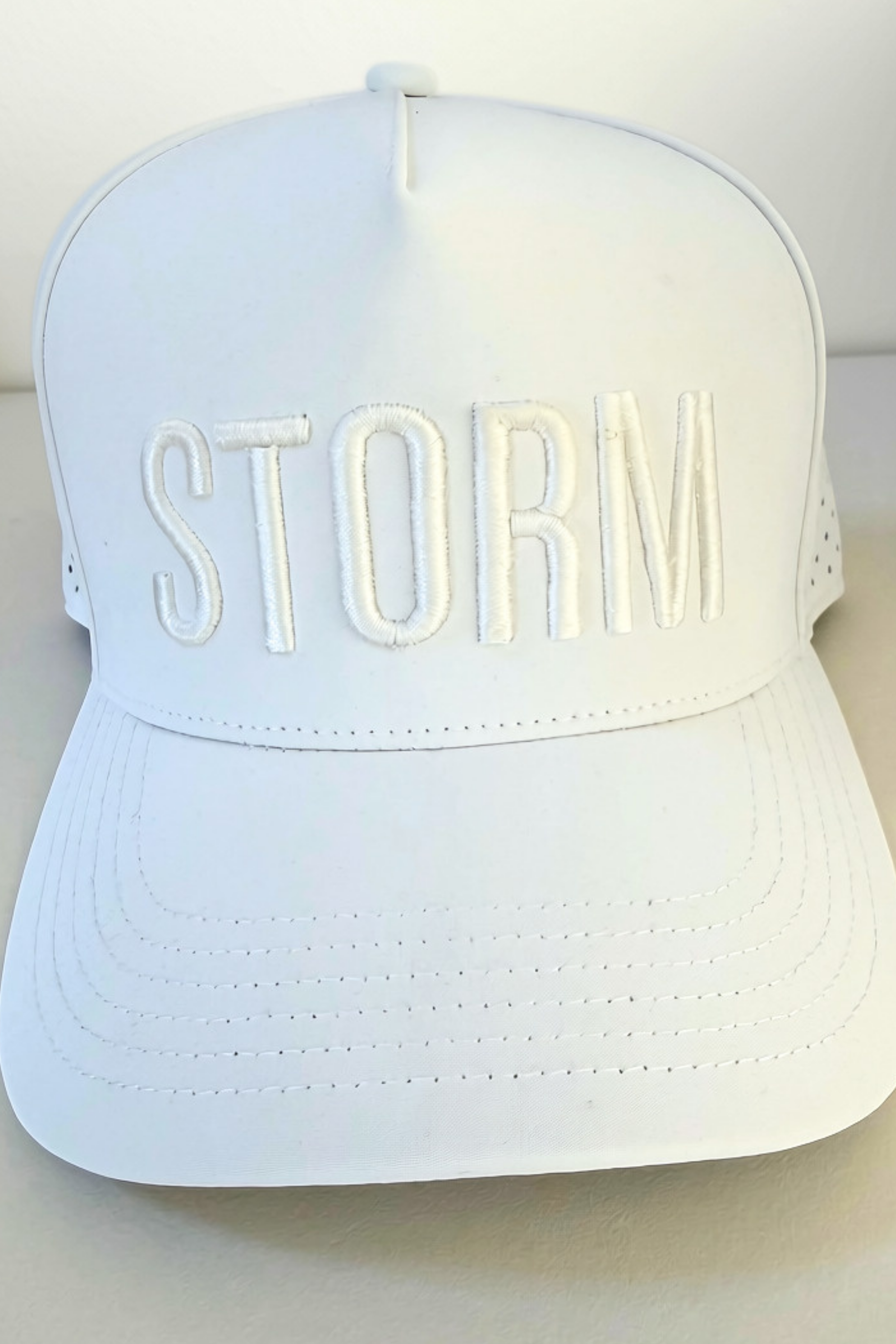 A white structured baseball cap with the word 'STORM' embossed in matching white letters across the front, photographed against a plain light background.