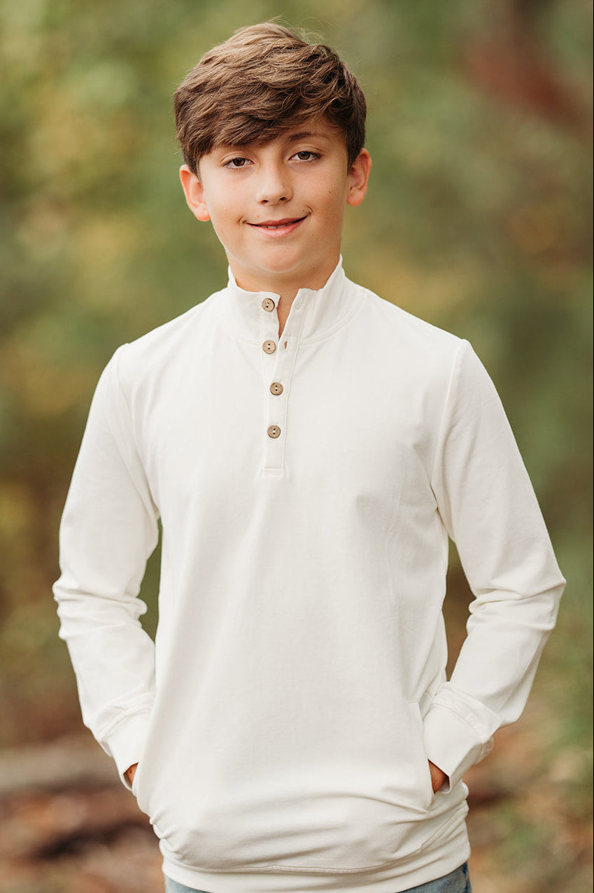 Young boy wearing a cream long-sleeve pullover shirt with buttons and pockets outdoors