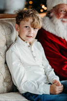 Young boy wearing a cream pullover sitting next to Santa Claus on a festive background